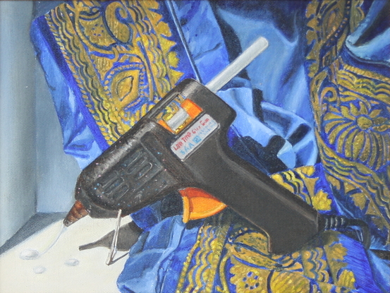 A black and orange hot glue gun resting against a tumbled piece of blue and gold silk.