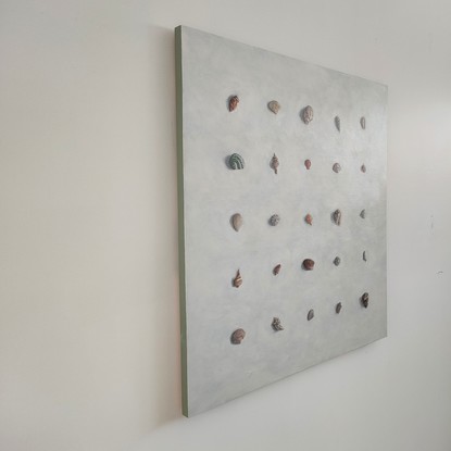 Sea shells of various shapes and sizes painted in rows to form a square on the board. The shells are soft muted colours on a neutral off white textured background. 