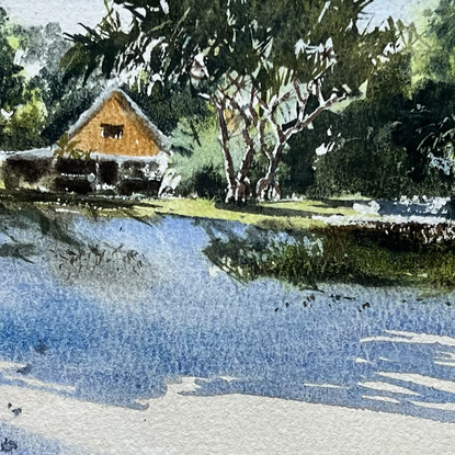 A view from the beach of a little cottage nestled amongst the trees with long shadows of the trees in the foreground.