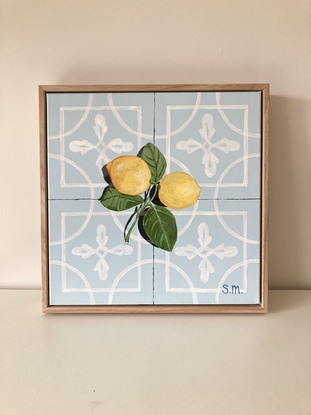 Two lemons, attached to their stems and resting on a powder blue encaustic tile background, accented by a contrasting shadow