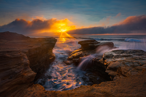 A beautiful beach at sunrise with rugged rocks and crashing waves.