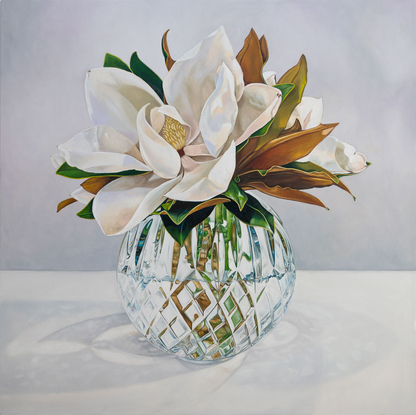 A large white magnolia flower and leaves of green and gold, in a cut crystal round bowl shaped vase. The background is a light grey white colour. The painting is framed by a light coloured wooden floating frame.