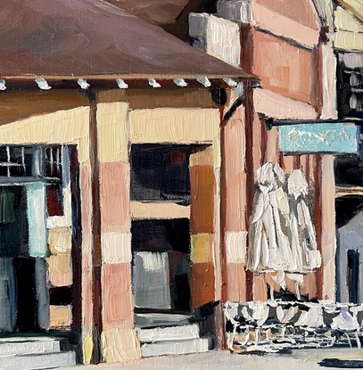 A street scene of the Strand, the main road through Croydon village. It shows the distinctive old post office which are prominent and iconic through many suburbs of the inner west of Sydney. The afternoon sun creates strong shadows off the two storey building of the street. To the left, a pair of a much longer row of palm trees frame the scene. 