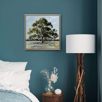 A grand tree lite in sunlight with a border of trees behind. A blue sky peeks through the leaves. 