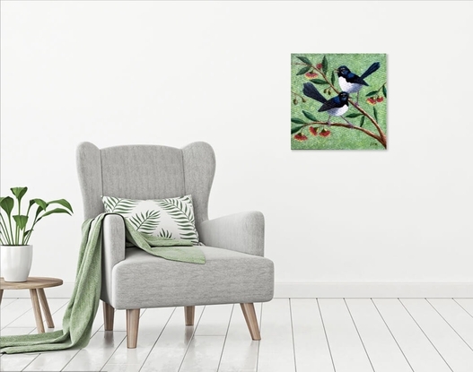 Two beautiful Willy Wagtails sitting on a eucalyptus tree with red and yellow gum blossoms. The background is a pale green speckled colour, with specks of yellow blossom sifting through the air.  The two birds appear to be in conversation.