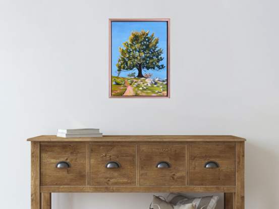 A large tree standing in the centre of a field on a hill with a pathway to the top of the hill, under a clear blue sky