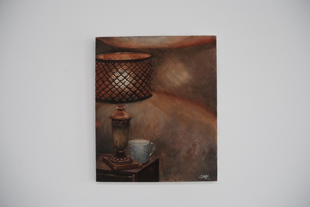 A retro copper lampshade sits atop a bedside drawer,  illuminated by a household table lamp. There is a coffee mug at the base of the lamp and the picture is flooded with soft, warm light.