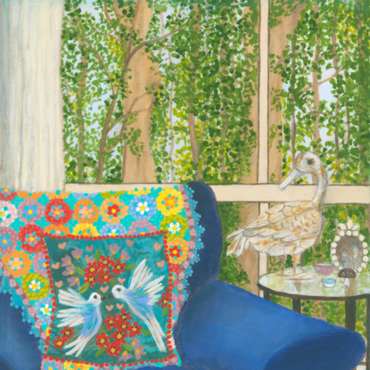 Interior scene with a rusty duck ornament on a glass side table, next to a blue arm chair and a rainbow crochet blanket hanging over the back behind a blue cushion featuring white birds and pink and red flowers. Against a window backdrop featuring leafy green trees