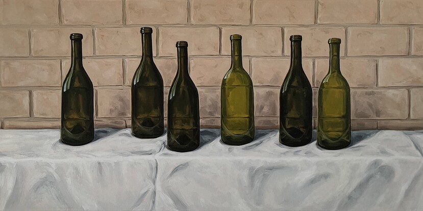 Six empty green wine bottles on a white tablecloth in front of a brick wall.