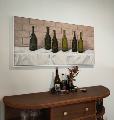 Six empty green wine bottles on a white tablecloth in front of a brick wall.