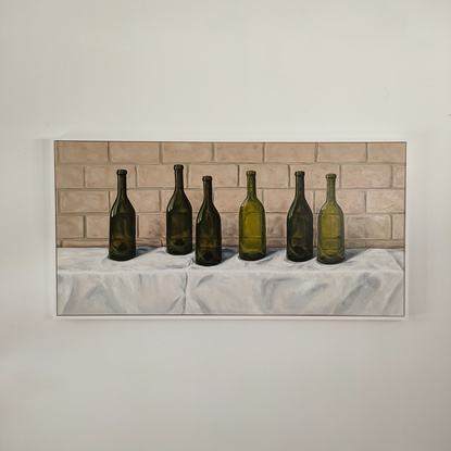 Six empty green wine bottles on a white tablecloth in front of a brick wall.