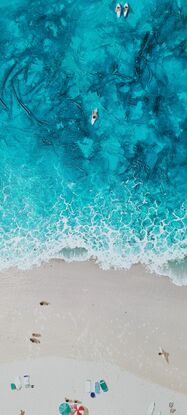 Surfers come and go from the ocean and sunbathers stretch out along the beach to enjoy the sun.