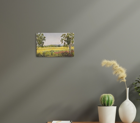 a landscape under light pastel skies with distant ranges are vast field of cheerful yellow canola in the spring season with gumtrees and roadside vegetation in the foreground and some birds flying over the countryside.