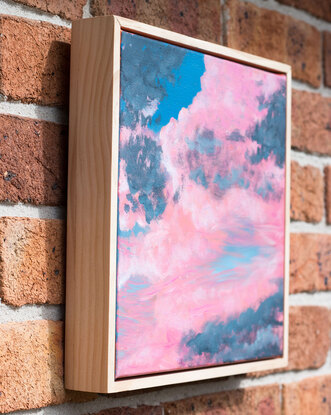 Fluffy pink and grey clouds float in front of a blue sky