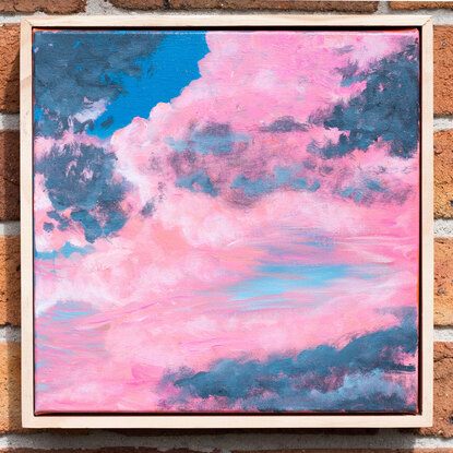 Fluffy pink and grey clouds float in front of a blue sky