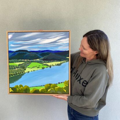 A view of the Hawkesbury River from Hawkins Lookout Point under a cloudy moody grey sky. There are trees in the foreground directly underneath the viewer and trees lining the river and dark blue and green hills and trees in the distance. 