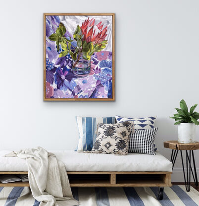 A king protea in vase sitting on bright floral retro sheet in purples and blues