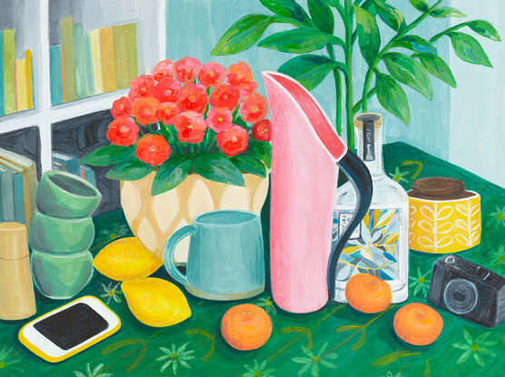 Table scene of pink Fink jug, gin bottle, potted plant, mug and lemons and mandarins. An i-phone sits on the table on the left on a green tablecloth and a camera and sugar bowl are on the right hand side. There is the suggestion of a bookshelf in the background.