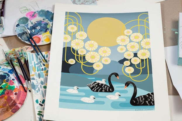 A family of Australian black swans swim gracefully on a moonlit river. The edges of the painting are filled with stylised circular Eucalyptus blossoms with swirling yellow stems. A pale golden moon hangs in the background. One of the cygnets rides on its mothers back while 3 other baby swans are in the water beside the parents.