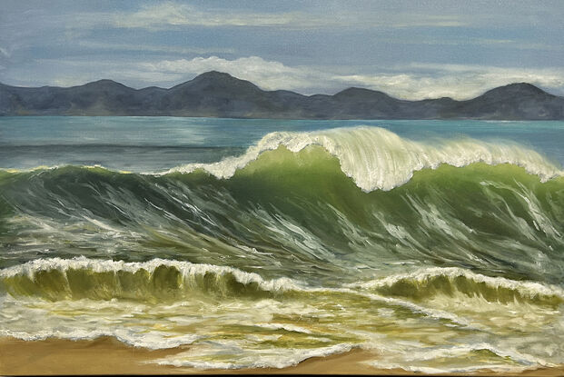 Large wave cresting on beach with mountains in background.