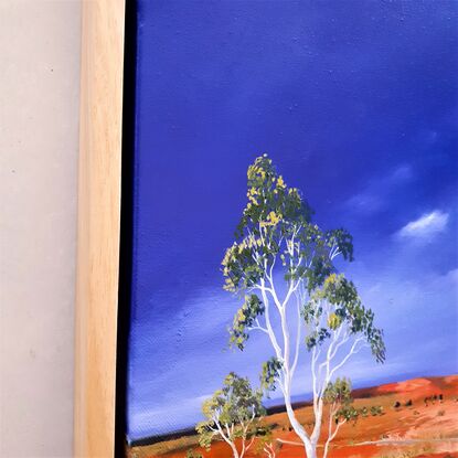 Australian landscape in yellows, oranges and deep blue sky with a road and gum trees, dust storm coming