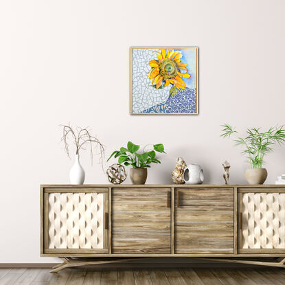 A single sunflower, facing towards the viewer, is created using watercolour. It sits in a blue and white detailed vase, on a blue and white tablecloth - both created using collaged paper. The background is a white, geometric, marble-like texture, also created in collaged paper. 