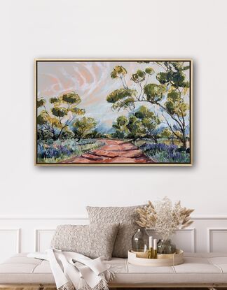 Spring grasses edge a red dirt track that weaves through mallee trees. A pink and blue sky have white whispering clouds. 