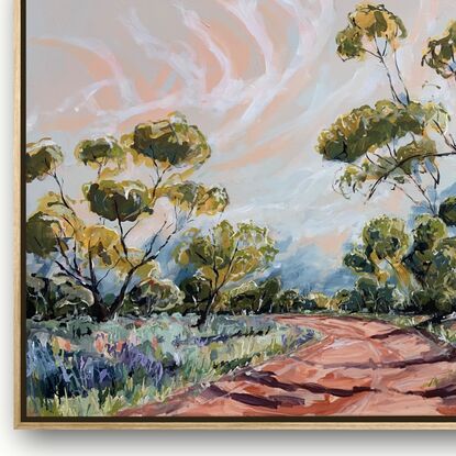 Spring grasses edge a red dirt track that weaves through mallee trees. A pink and blue sky have white whispering clouds. 