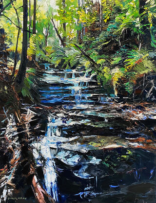 Vertical view of a waterfall running down rocks towards the viewer. There are bright green ferns at the top and on either side of the waterfall, towards the bottom, there are dark brown rocks with the light blue water, reflecting the sky.