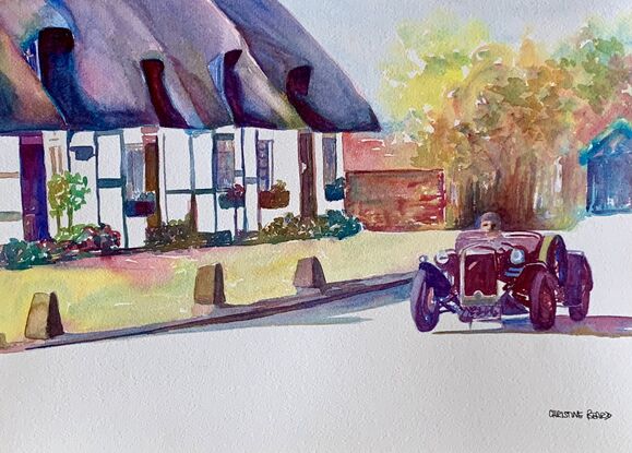 Vintage classic car drives past a row of thatched cottages.
