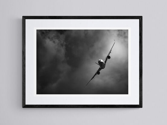 A black and white photograph of the Airbus A350, flying towards the photographer, in a steep right-hand turn in front of a dramatic cloudy background.