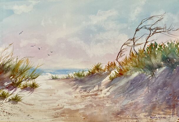 Sand dune in violet shadow in foreground with grasses on top, blue ocean behind, cloudy sky 