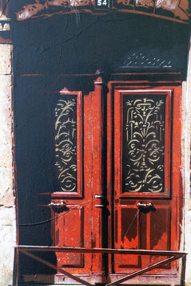 a woman walks past a set of old red doors in France