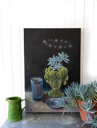 A head shaped planter with limes carved into the head as if hair. A circle of stars above the head and blue embossed glass. Dark background.