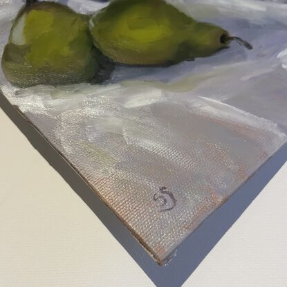 Two ripe green pears and some strawberries in a white bowl, with their reflections in a metal tin. On a white tablecloth.