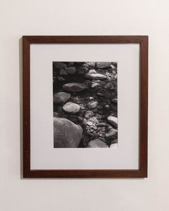 Photograph of stones in a river bed. Water reaches halfway up the larger ones as sunlight plays across them in patches.