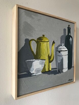 four vintage objects sit on a mid grey surface. A small white bowl, a yellow enamel coffee pot, a lidded white enamel canister and a taller olive green bottle. the background is a light grey