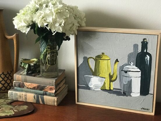 four vintage objects sit on a mid grey surface. A small white bowl, a yellow enamel coffee pot, a lidded white enamel canister and a taller olive green bottle. the background is a light grey