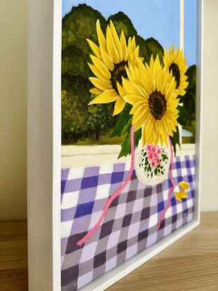 vase of 3 sunflowers on a purple gingham table cloth against a window view hinterland inspired landscape scene