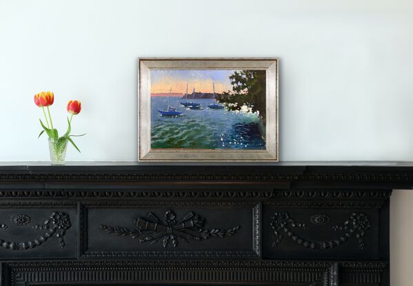 Four boats on the harbour waters, sunlight behind a tree sparkling in the water. 