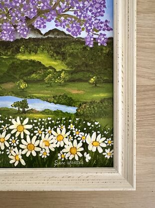 Jacaranda tree above a field of white daisies set against a a hinterland inspired backdrop with rolling green hills and blue sky