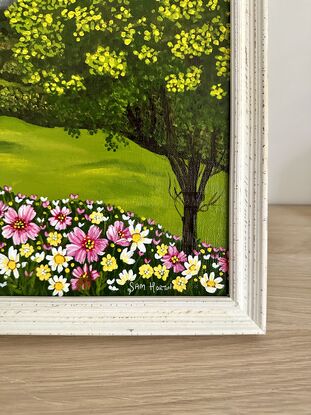 golden wattle tree and a field of pink yellow and white wild flowers against a landscape backdrop of rolling green hills and a blue sky