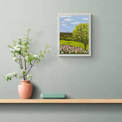 golden wattle tree and a field of pink yellow and white wild flowers against a landscape backdrop of rolling green hills and a blue sky