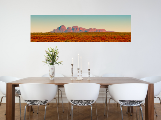 Panoramic photo of Mount Olga in Australia's Northern Territory, featuring stunning mountain range backdrop against rugged, red-hued foreground.