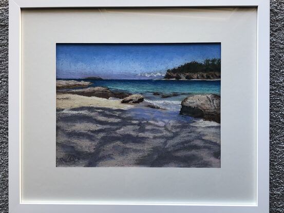 Tree shadows on sand with turquoise water and  headland in the background.