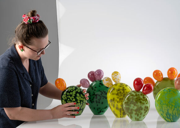 Upright glass sculpture, a large green flat leaf with five rounded yellow buds attached on the top.