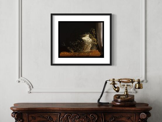 A vintage yellow ceramic jug sits to the right of frame on an antique wooden surface which stretches across the lower third of the image from left to right. The only light source is through an unseen window, to the right of the jug. The window is partly out of frame and partly obscured by a white thick cotton curtain. A shadow runs diagonally through the frame from upper right hand side to lower left, throwing most of the upper left corner of the image into darkness. There are no flowers in the jug, however, long, thin, complex strands of zigzag wattle with small yellow balls of flower are loosely wrapped around the jug, both embracing it and forming an impenetrable barrier around the jug. The strands disappear into the shadow, and small balls of dropped wattle flowers are scattered around the jug.