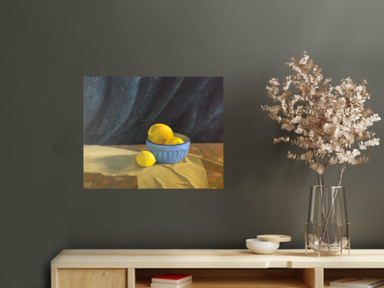 Three yellow citrus fruits, in a blue ceramic bowl with blue drapery in the background