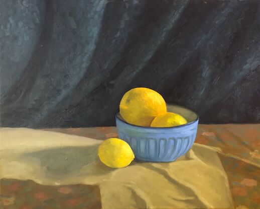 Three yellow citrus fruits, in a blue ceramic bowl with blue drapery in the background