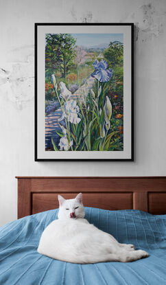 Purple Iris in the foreground with a path leading to Monet's house, lined with lush bedding plants and  trees, in soft lilacs, pinks and greens against a pale blue sky, on a portrait orientation canvas with a tradition carved cream coloured frame.